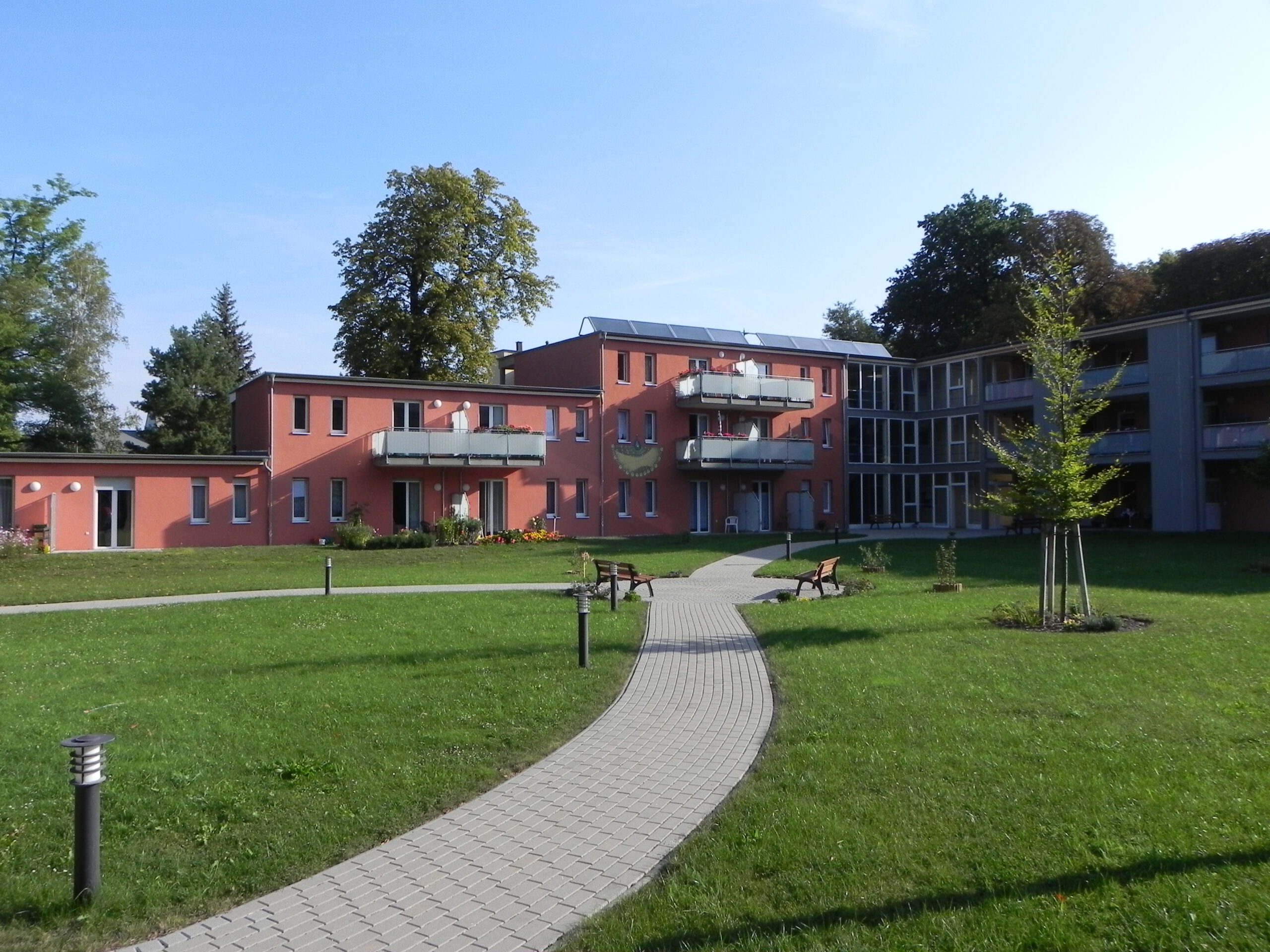 Moderner Gebäudekomplex mit Balkonen, davor ein gepflasterter Weg durch eine große Rasenfläche.