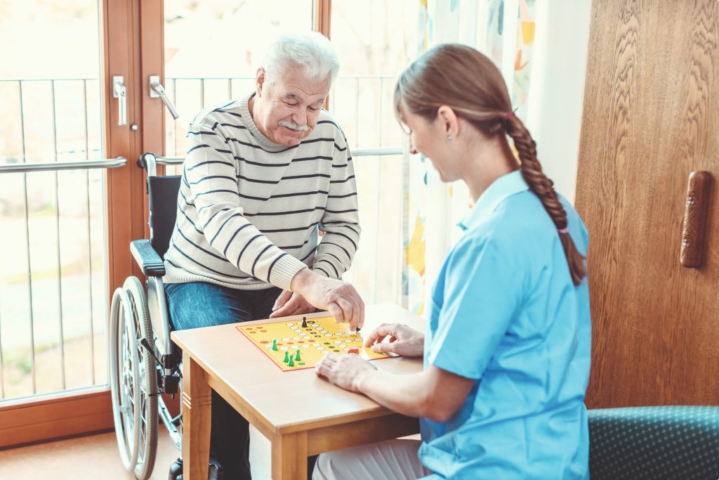 Ein Senior spielt ein Brettspiel mit einer Pflegerin