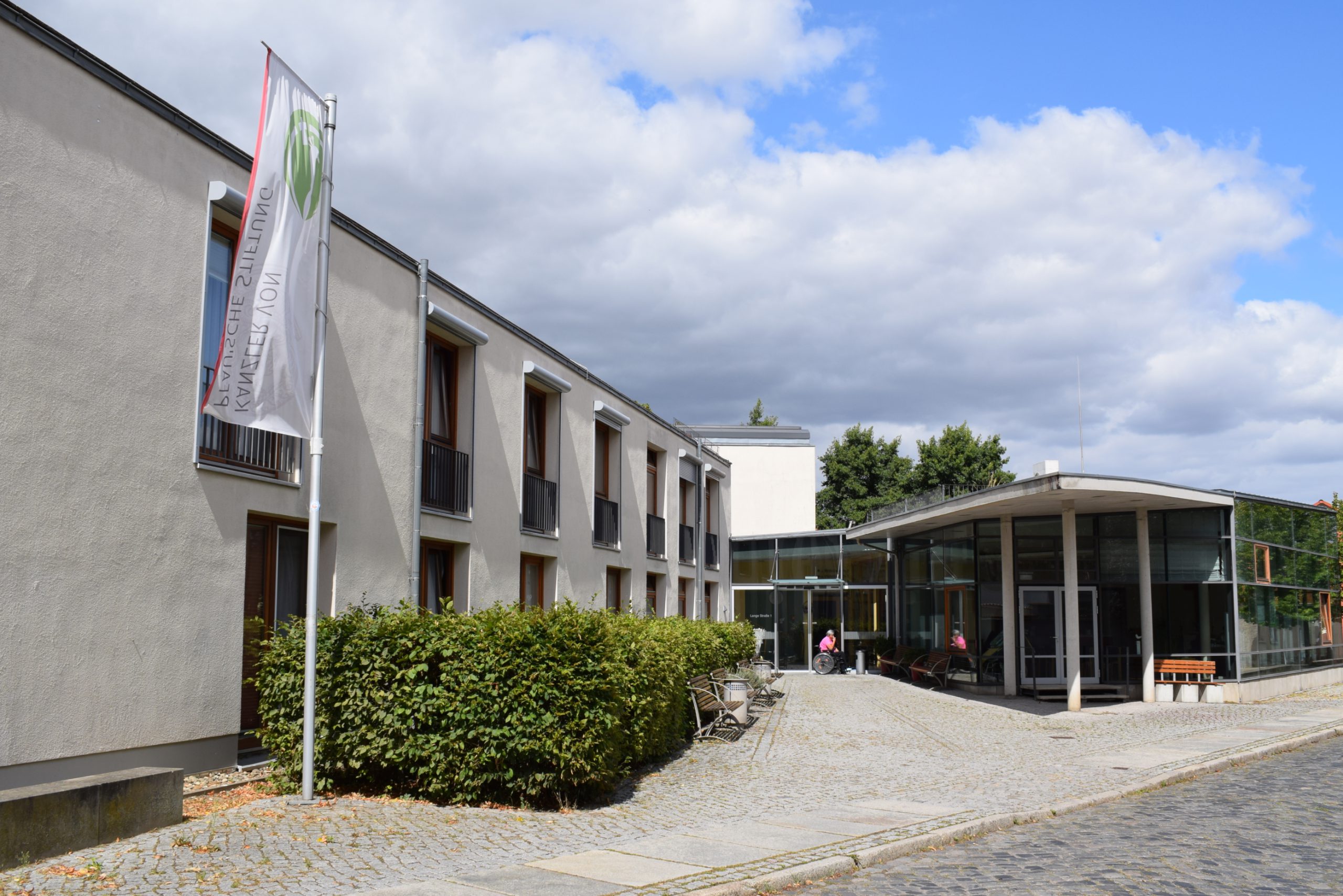 Eingangs vom Nicolaistift in Ballenstedt mit einer Fahne der Stiftung. Am blauen Himmel sind ein paar Wolken.