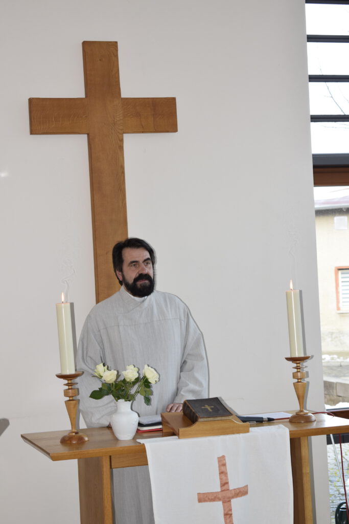 Pfarrer Nürnberg hält eine Predigt am Altartisch mit zwei Kerzen und der Bibel auf dem Tisch