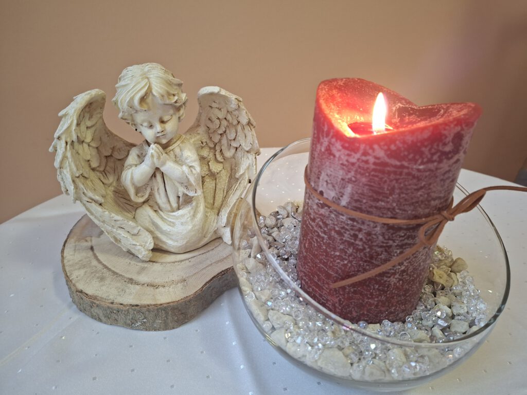 Auf einem Tisch stehen eine Engelsfigur und eine rote Kerze brennt.