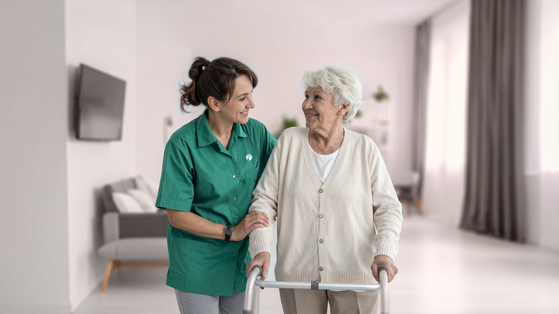Eine Pflegekraft unterstützt eine Patientin in deren Wohnung beim Laufen.
